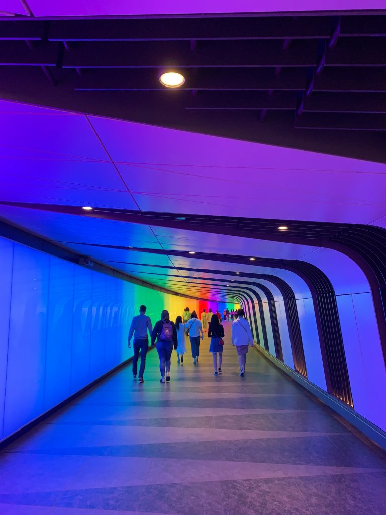 People walking through a colourful lit tunnel